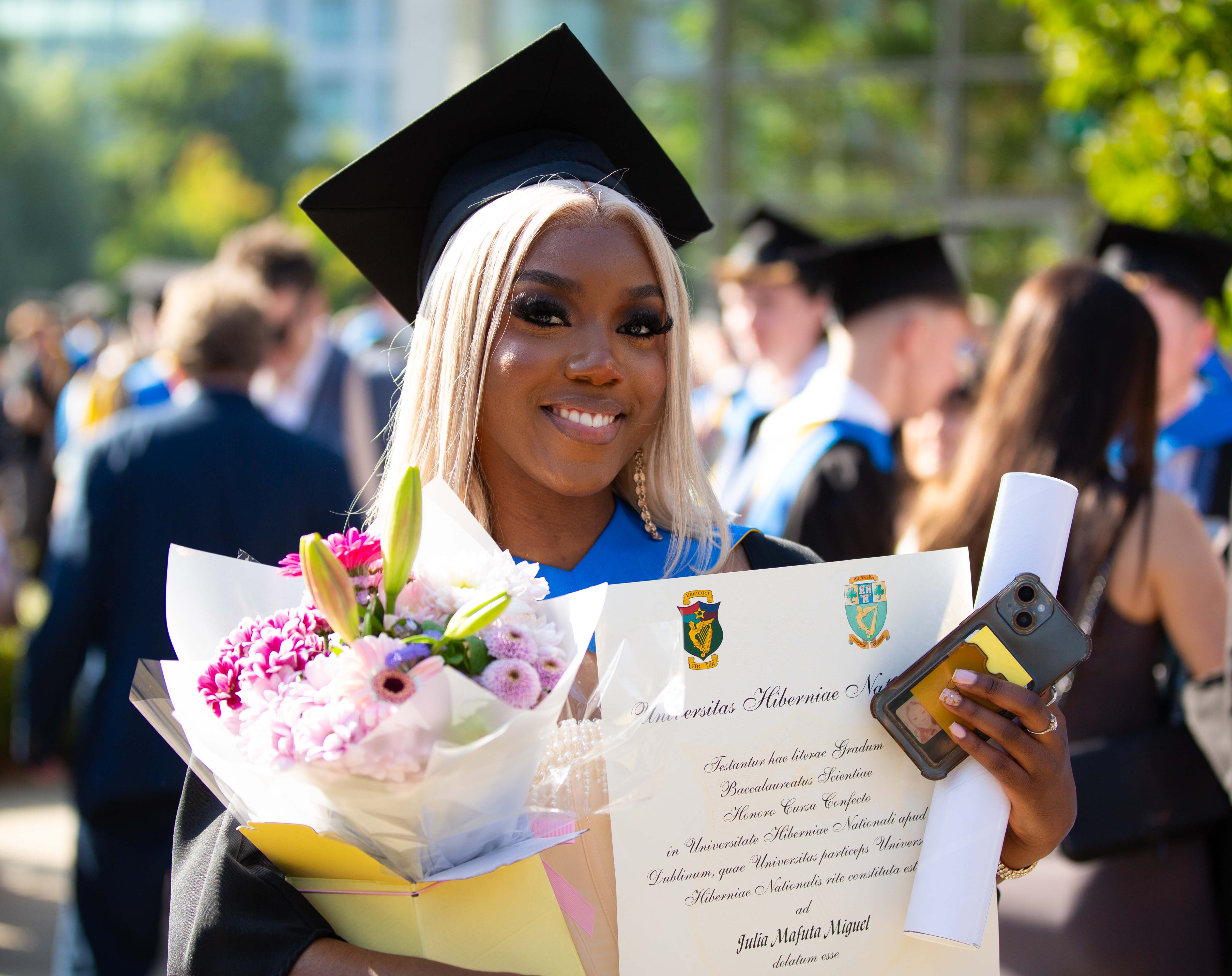 A smiling student holding scroll and flowers
